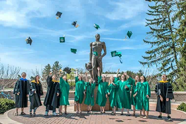 Students standing in front of Spartan statue in caps and gowns throwing their hats in the air